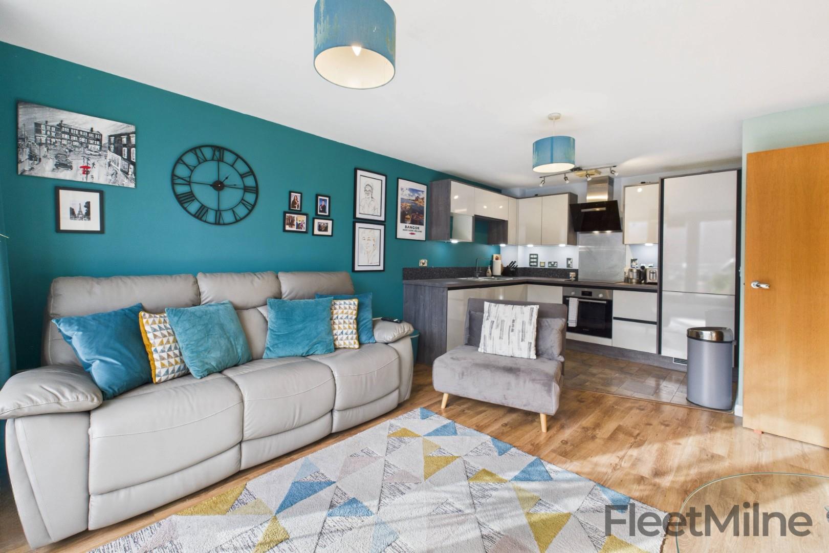 Contemporary open-plan living area in a Birmingham rental apartment featuring a teal accent wall, modern kitchen and stylish furnishings — FleetMilne lettings agent in Birmingham City Centre.